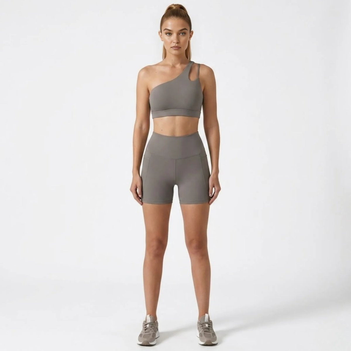 Front view of woman wearing Kouvr grey asymmetrical one shoulder sports bra and high waisted biker shorts activewear set.