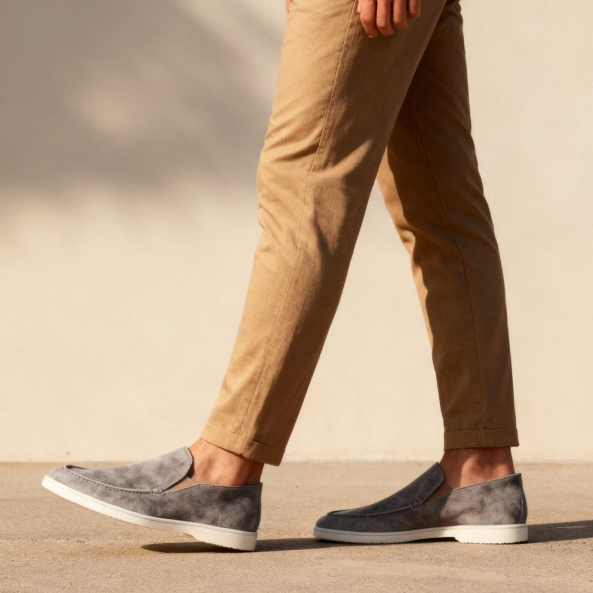 A side view of a man walking in grey Italian suede slip-on ralph sneakers with a white sole, showcasing the shoe's profile in motion.