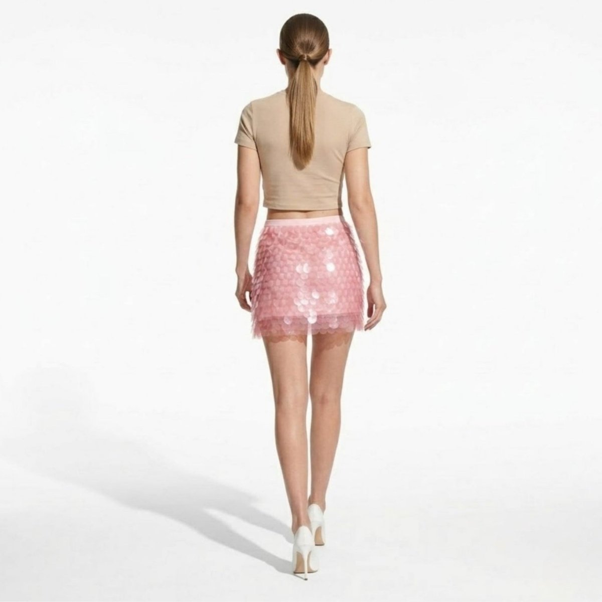 Back view of a high-waisted pink sequin skirt showing the layered disc texture, banded waist, and flattering mini length.
