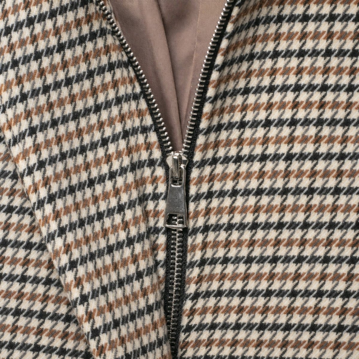 Macro shot of the open front placket of a houndstooth jacket revealing the concealed silver metal zipper and smooth inner lining.