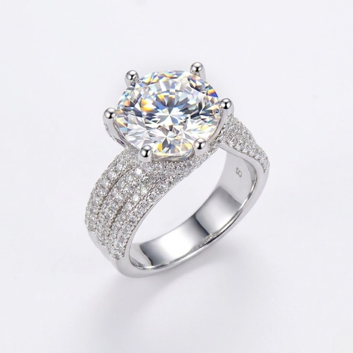 A 5 carat round brilliant moissanite engagement ring with a six-prong setting and a wide three-row pavé diamond band in platinum-plated sterling silver by Kouvr.