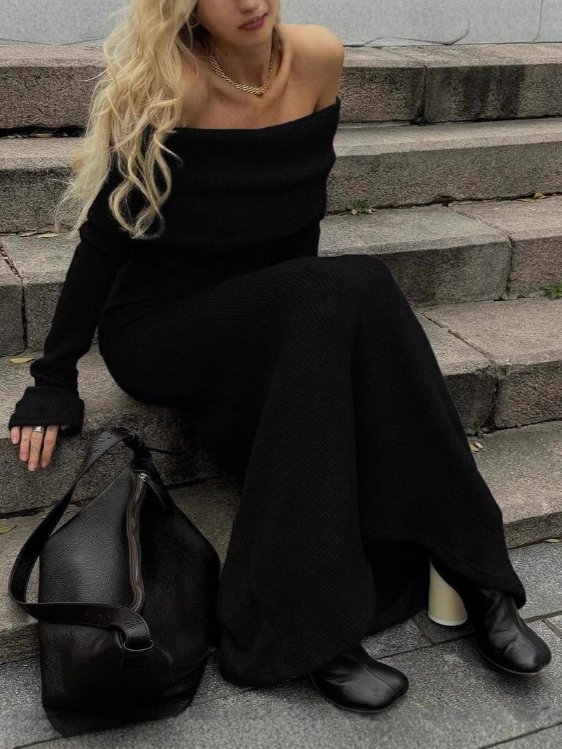 A woman sitting on stone stairs wearing the Kouvr Ingrid black off-the-shoulder knit maxi dress with black boots and a large black bag.