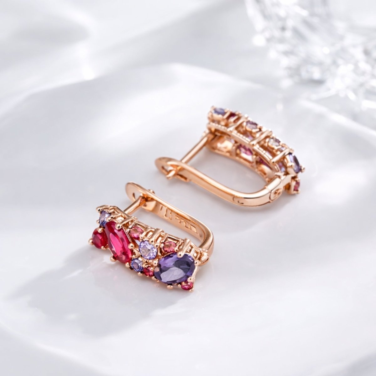 A pair of Kouvr Aileen 585 rose gold multi-gemstone earrings lying on a white ceramic plate, showcasing the leverback clasp and detailed craftsmanship.
