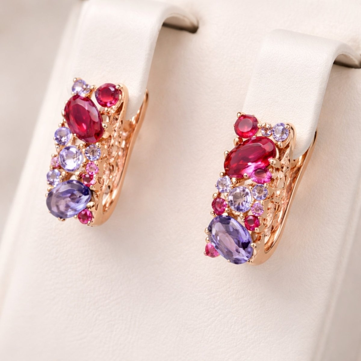 Kouvr Aileen rose gold gemstone huggie earrings displayed on a white jewelry stand, showing the side profile and vibrant colors of the zircon stones.