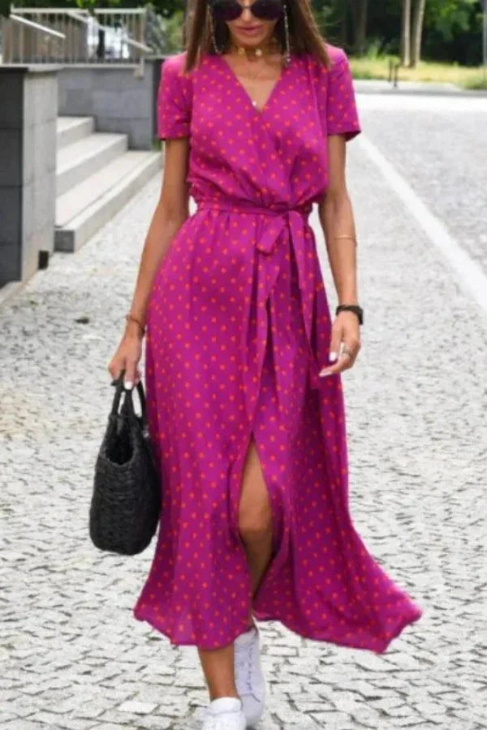 Woman walking in the Kouvr Aleia magenta and orange polka dot midi wrap dress with white sneakers