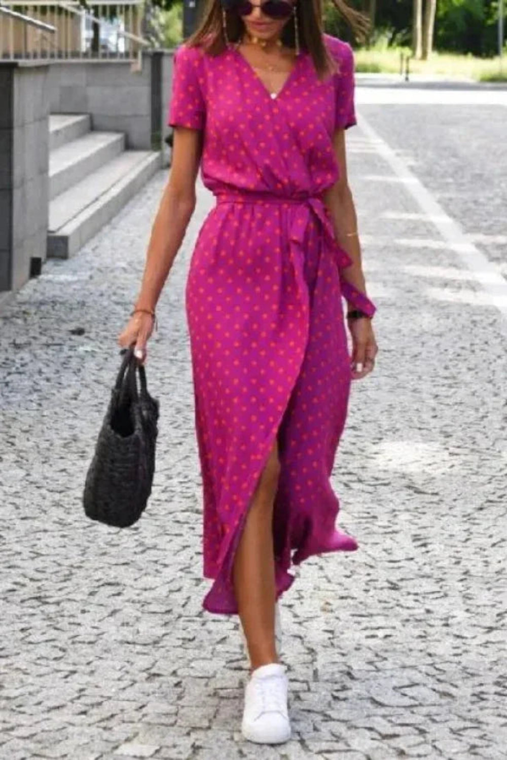 Woman walking in the Kouvr Aleia magenta and orange polka dot midi wrap dress with white sneakers