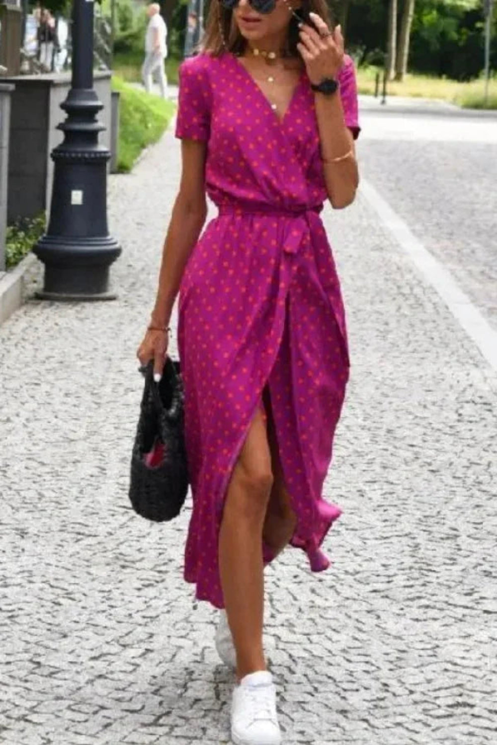 Woman walking in the Kouvr Aleia magenta and orange polka dot midi wrap dress with white sneakers
