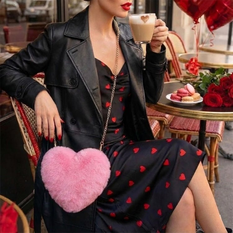 A stylish woman wearing a black heart-print dress and leather jacket sips a latte, with the pink fluffy Kouvr heart purse displayed prominently.
