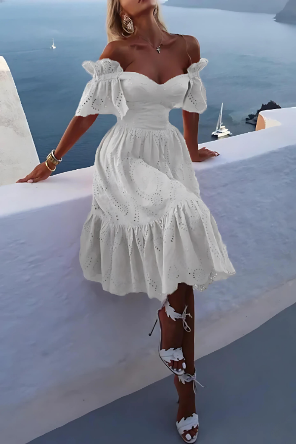 Model wearing the Kouvr Annie white eyelet midi dress on a balcony overlooking the ocean