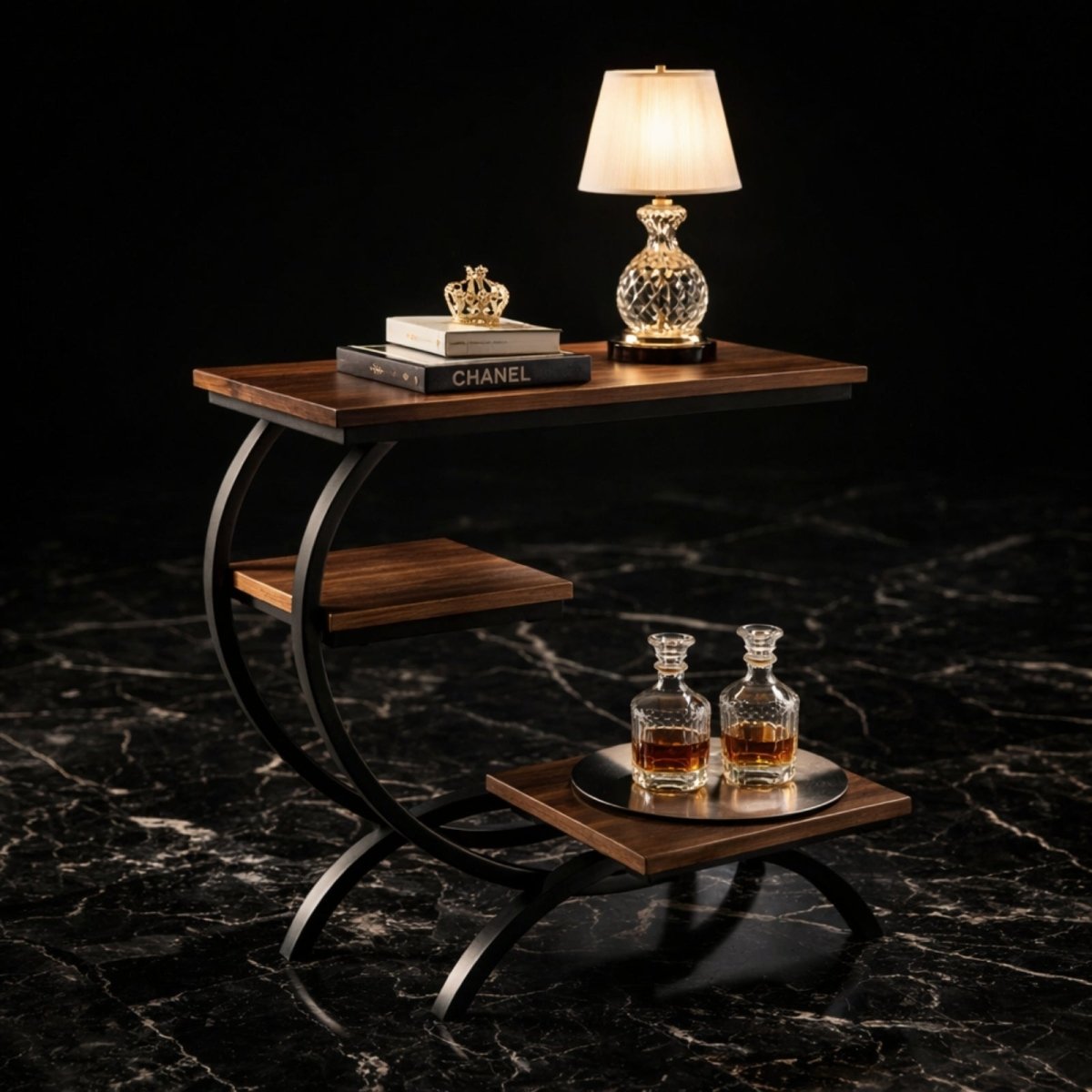 The Kouvr Arcadian 3-tier c-shaped end table in a walnut finish, styled in a dark room with a crystal lamp and books on a black marble floor.