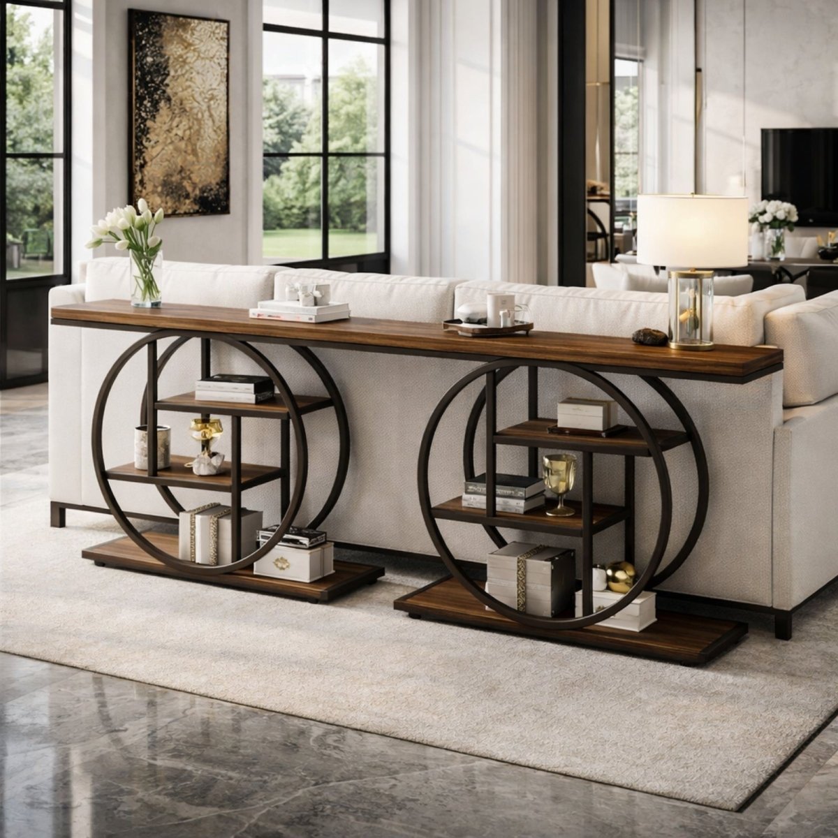 A long rustic wood and metal console table with two circular shelf bases from Kouvr, placed behind a white sofa in a bright, modern living room.