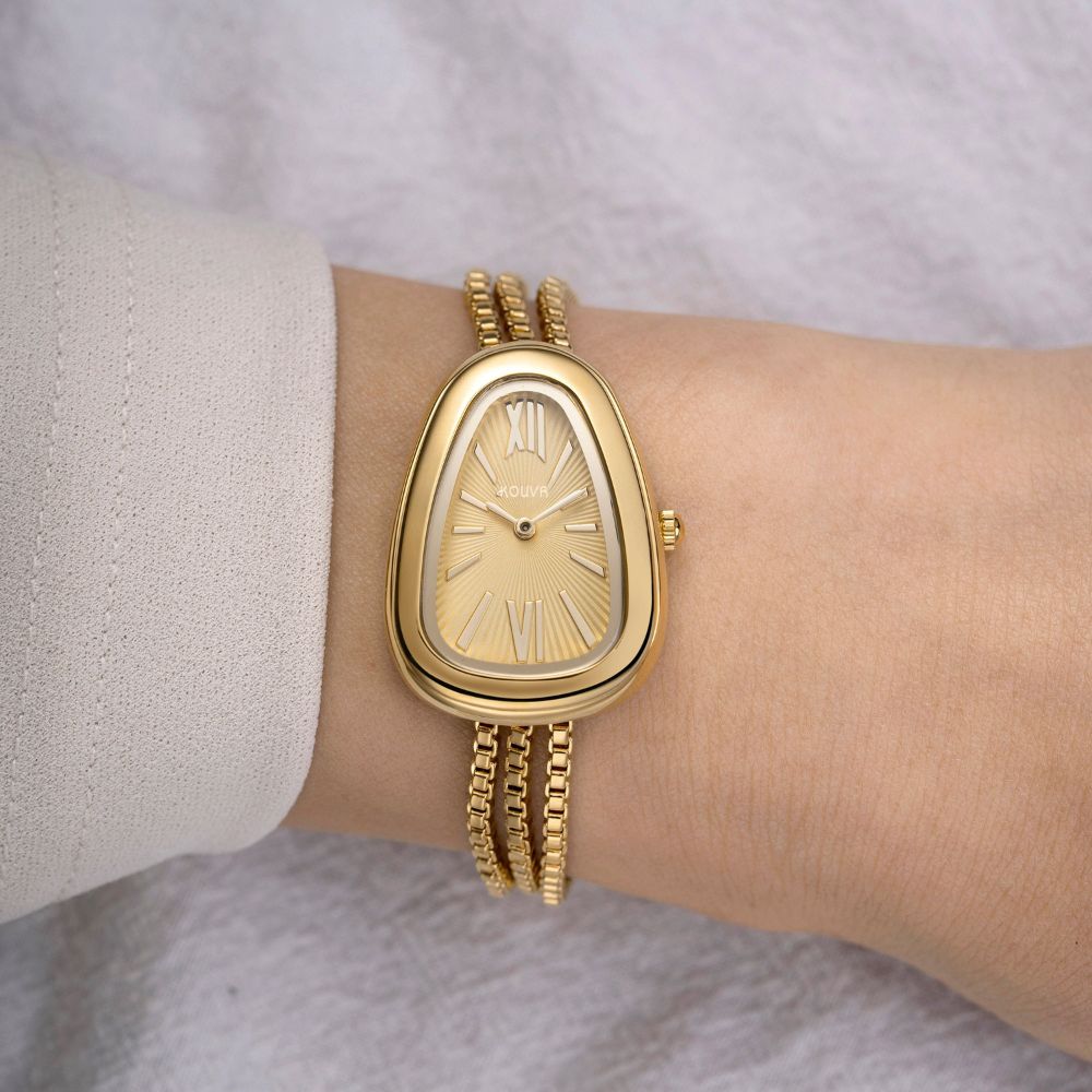 Gold kouvr wristwatch on a person's wrist with a light background