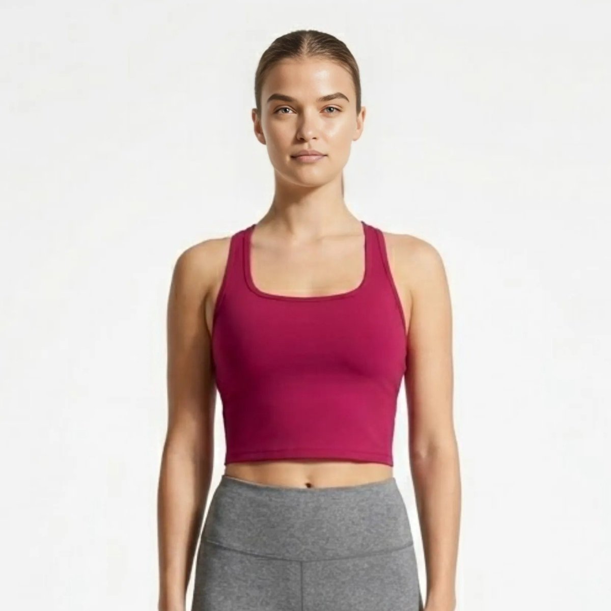 Woman wearing Kouvr berry red square neck cropped workout tank top and grey leggings facing forward