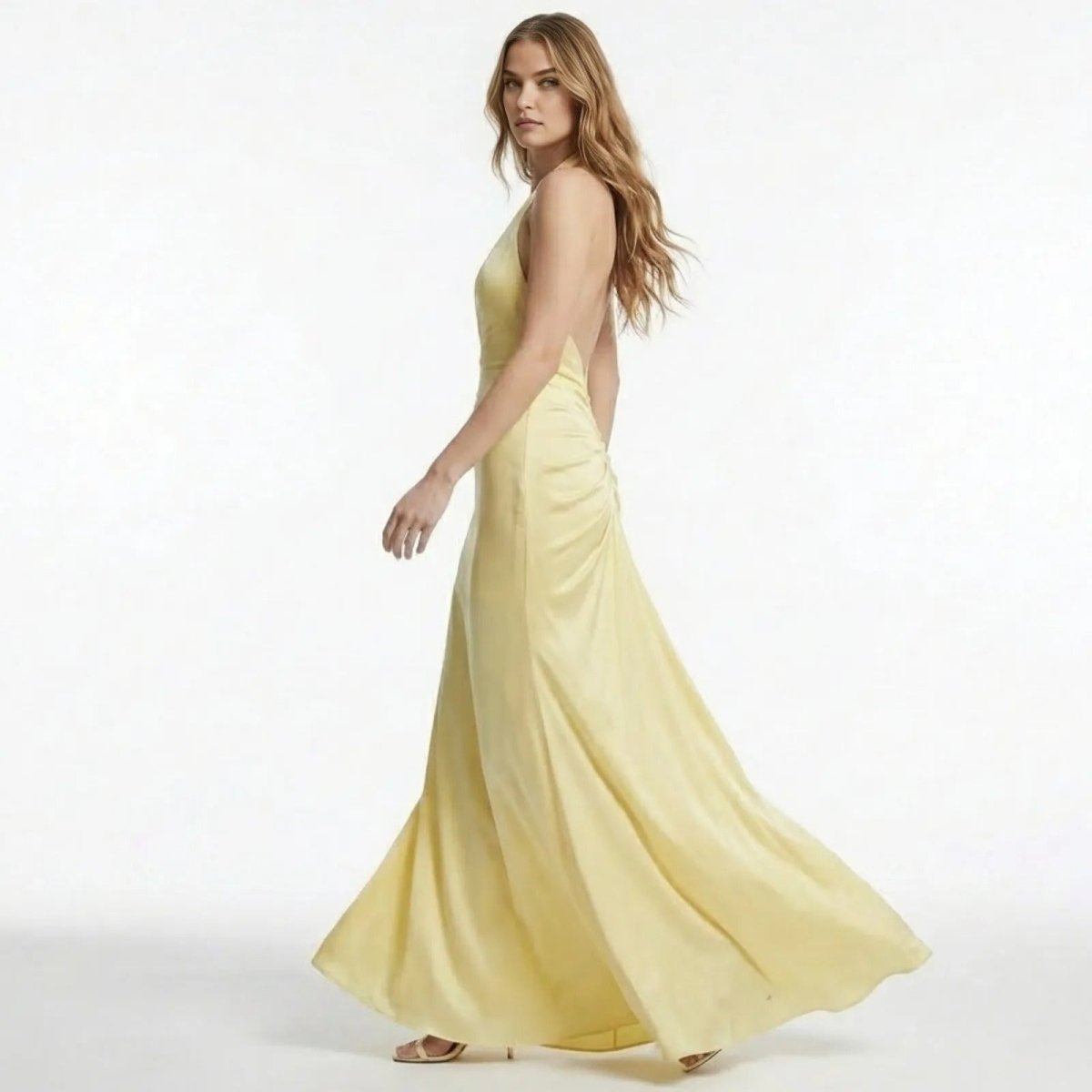 Side view of a model in the Kouvr Beverly light yellow backless maxi dress, showing the open back design and flowing mermaid skirt.