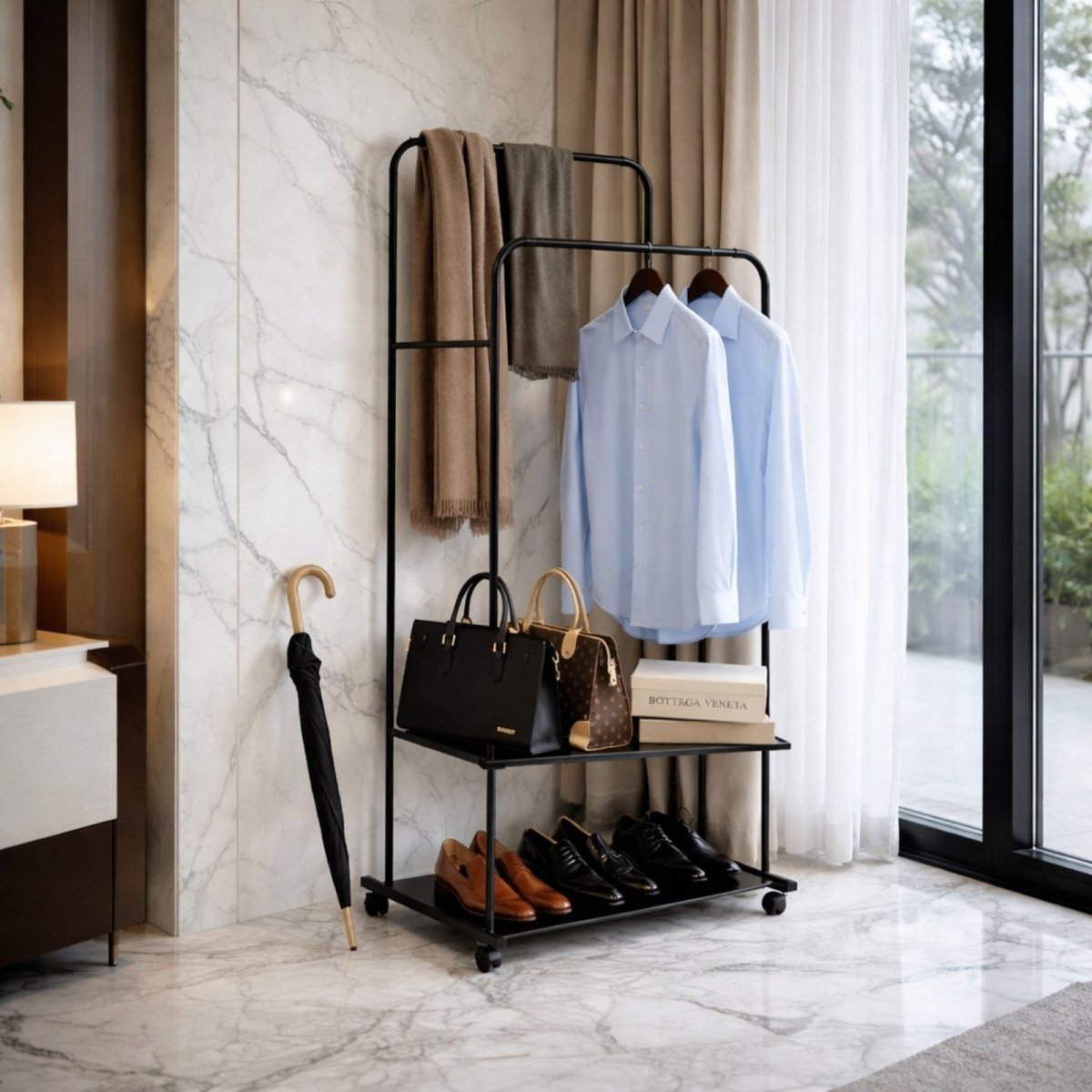 The Kouvr black garment rack used as an entryway valet stand, holding scarves, shirts, designer bags, and dress shoes on its shelves against a marble wall.