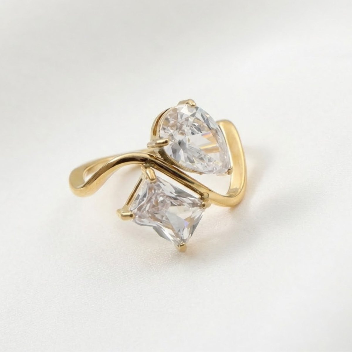 Kouvr Blanca Toi et Moi ring with pear and princess cut stones in 18k gold vermeil on a white satin background.