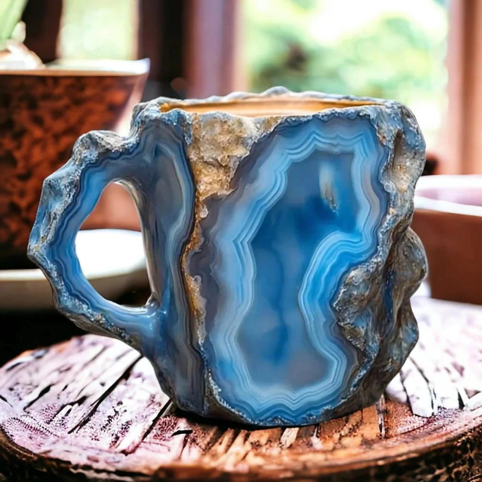 A unique blue agate geode coffee mug with a rough stone exterior sitting on a rustic wooden slice in a brightly lit room.