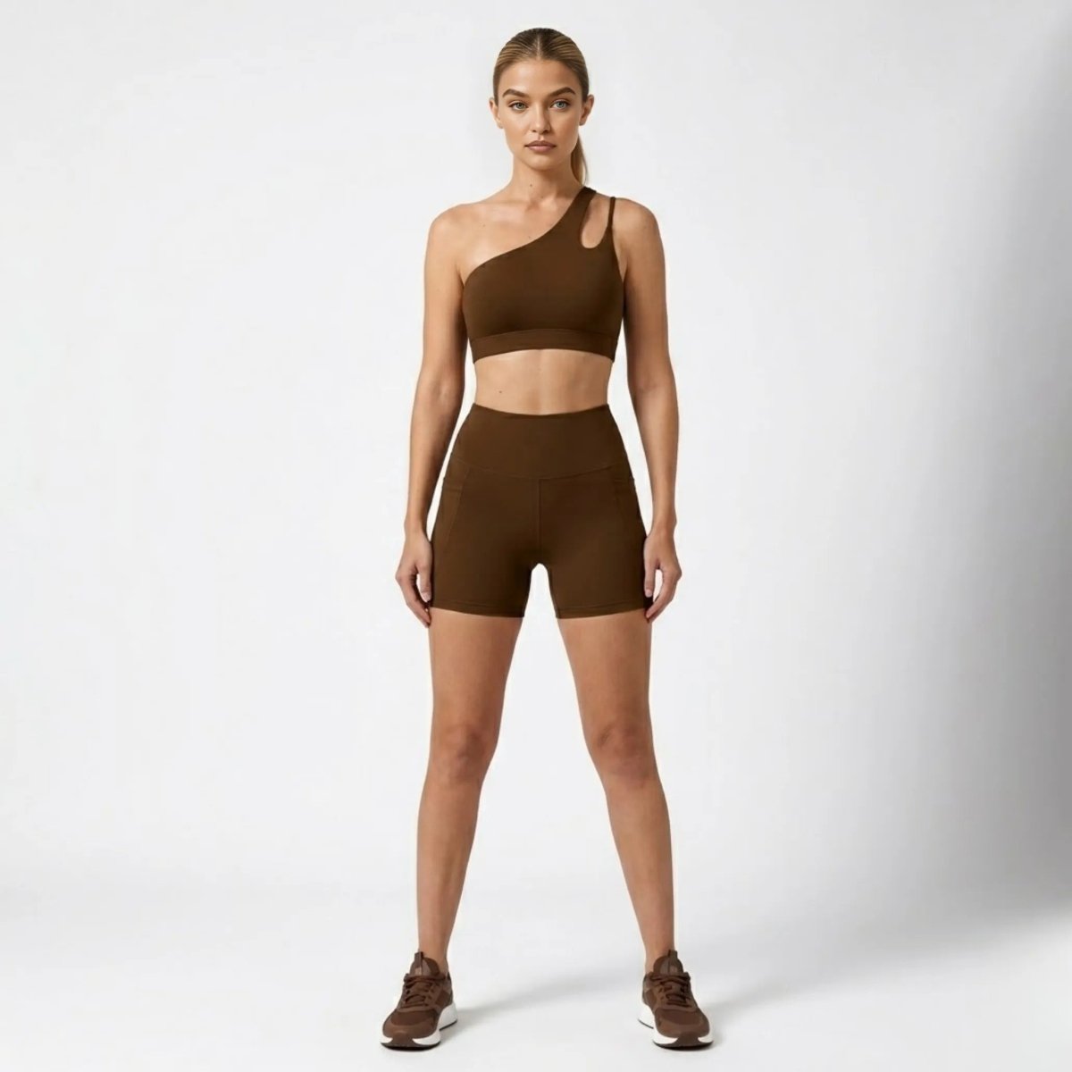 Woman wearing Kouvr dark brown one shoulder sports bra and high waisted biker shorts activewear set front view