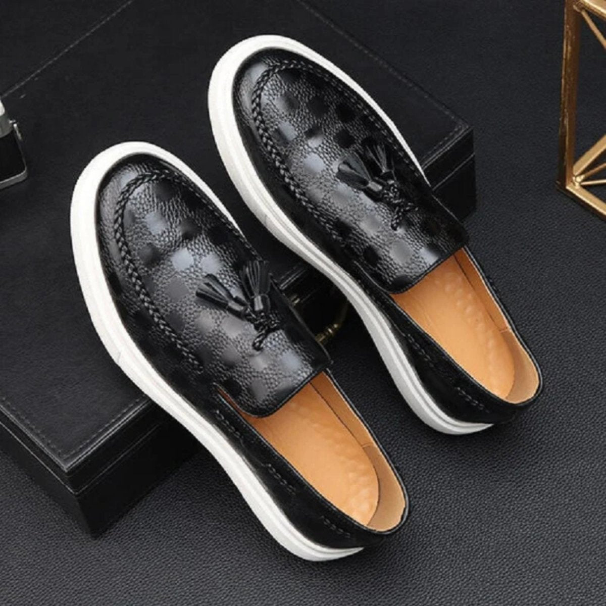A pair of Kouvr Carlo men's black embossed leather tassel loafers with a distinctive checker pattern and white sole, shown from a top-down angle.