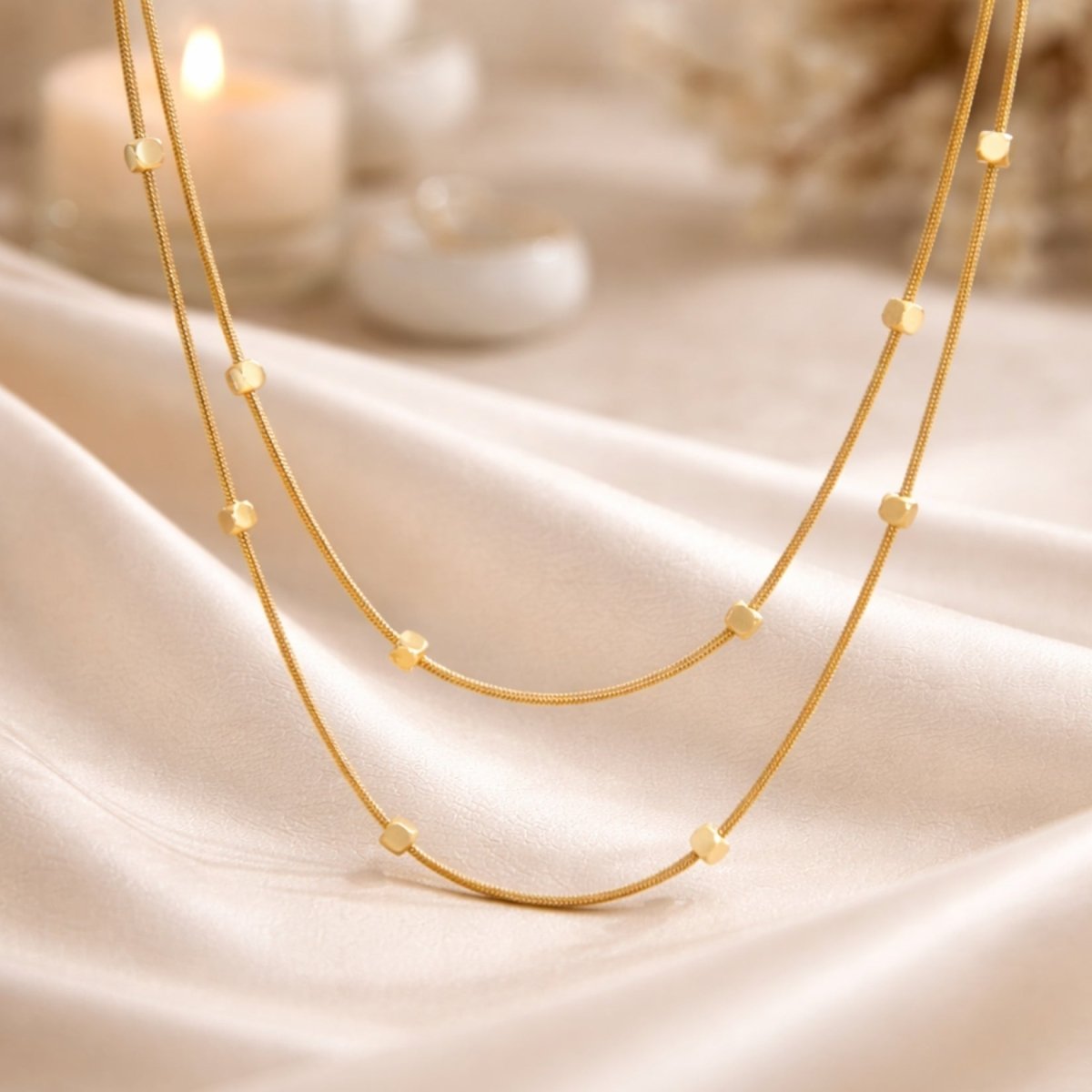 Close up of the Kouvr Celine double layered gold necklace resting on a cream-colored silk fabric with a soft-focus candle in the background.
Image 5 (Infographic):