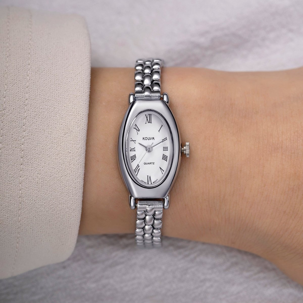 Silver watch with a white face and Roman numerals on a wrist, against a neutral background.