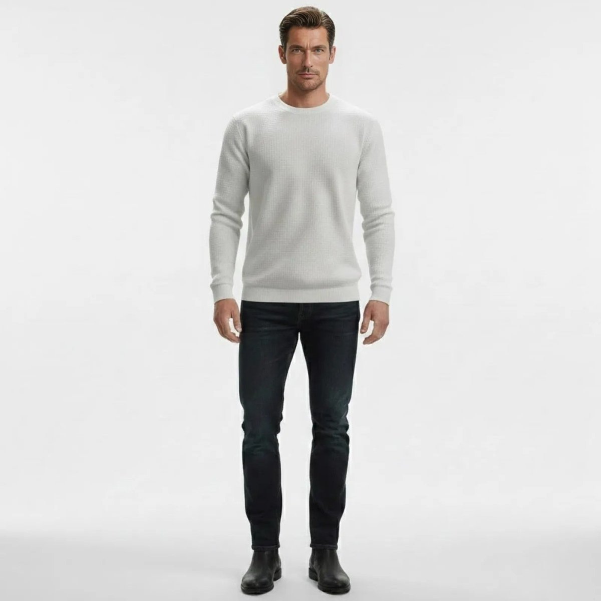 Man facing forward wearing Kouvr's chalk white slim-fit textured crewneck sweater with dark wash jeans and black boots.
