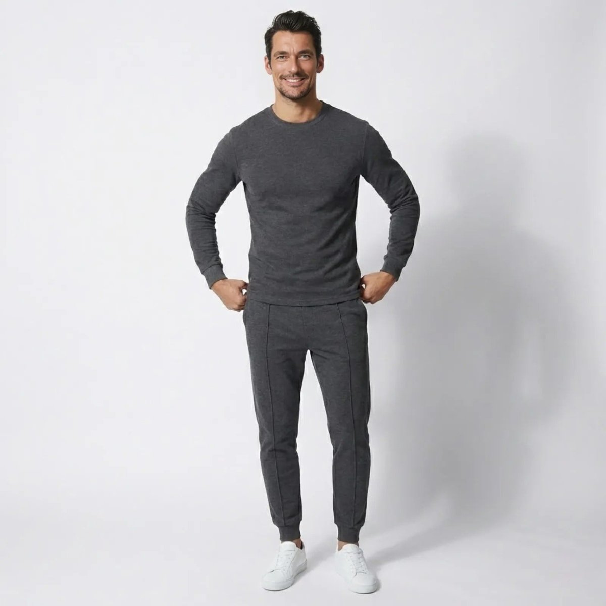 Man wearing the Kouvr Crue Knit Lounge Set in dark grey, smiling at the camera against a white background.

