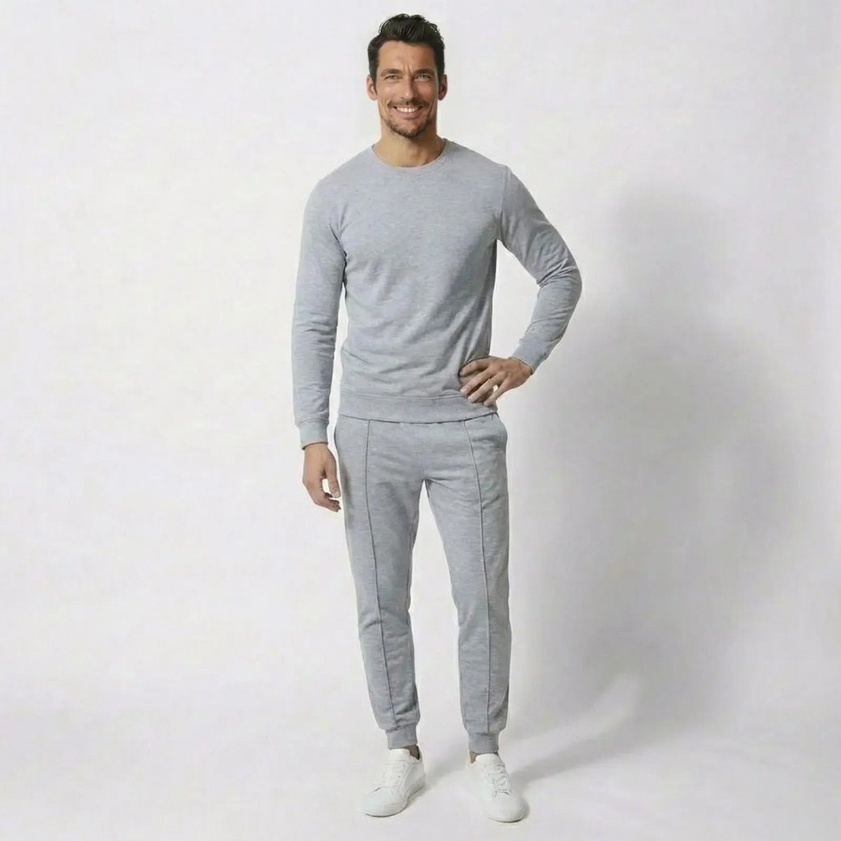 Man wearing the Kouvr Crue Set luxury heather light grey loungewear set, featuring a crewneck sweatshirt and tapered joggers, standing against a white background.