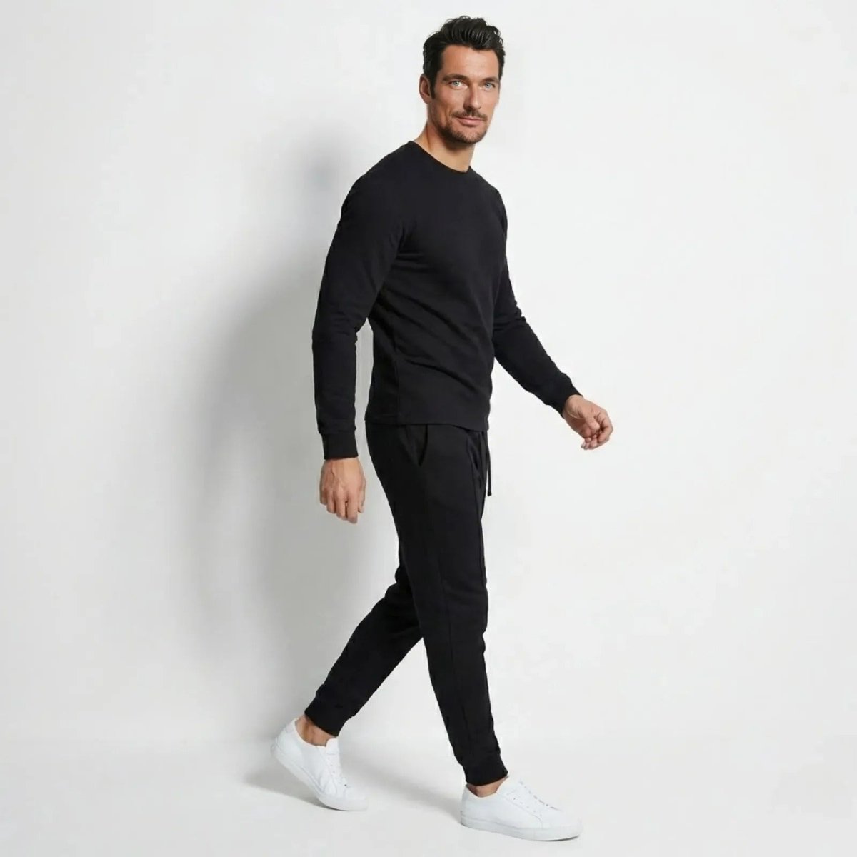 Side profile of a man walking in the Kouvr Crue black loungewear set, showing the athletic fit of the crewneck and joggers.