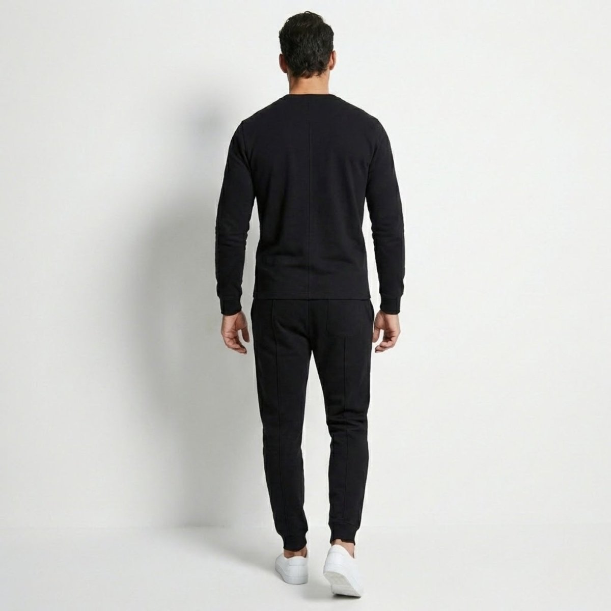 Back view of a man in the Kouvr Crue black sweatsuit, highlighting the vertical seam detail on the sweatshirt and tapered fit of the pants.