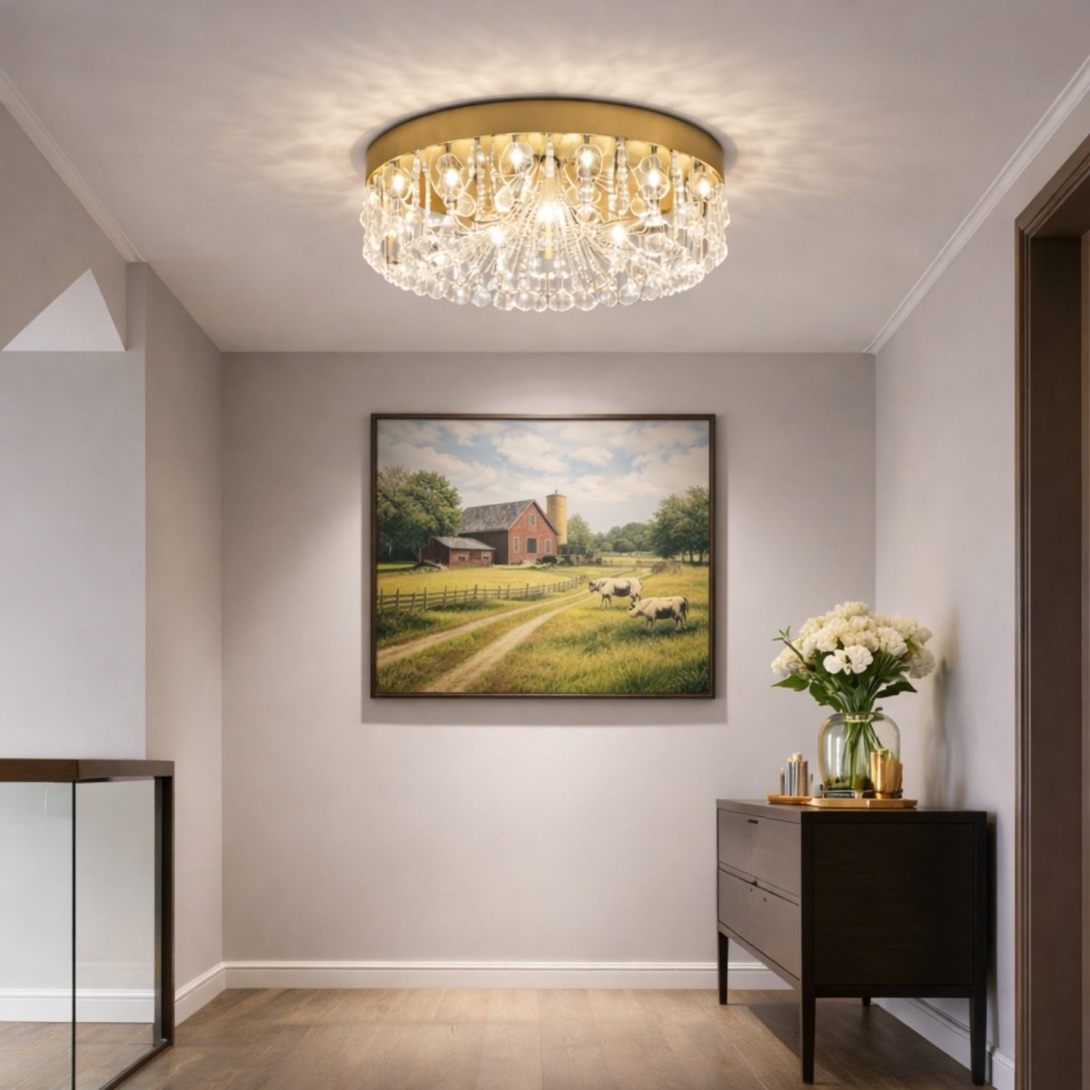 Entryway lighting idea with gold crystal flush mount fixture glowing with warm light against a neutral wall and landscape painting.