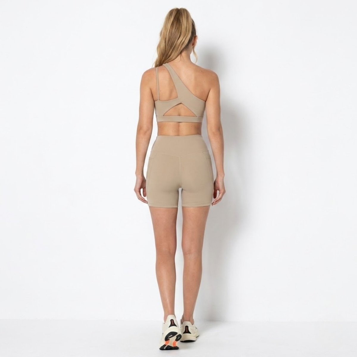 Back view of Kouvr khaki workout set highlighting the angular back cutout on the sports bra and form fitting biker shorts.