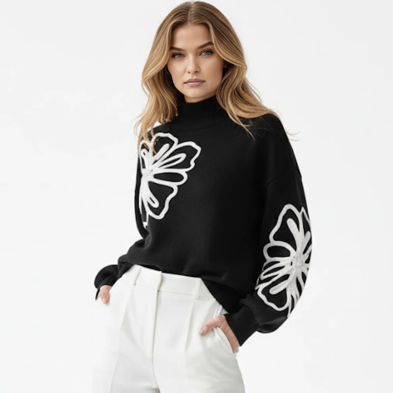 Model wearing the Kouvr Cynthia black mock neck sweater with large white floral embroidery on the chest and sleeve, styled with white trousers.