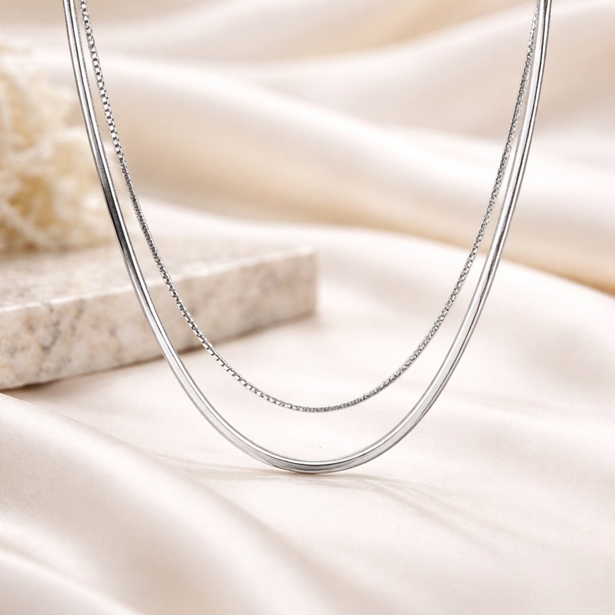 A detailed shot of the Kouvr layered silver necklace showing the texture of both the snake and box chains on a neutral background.