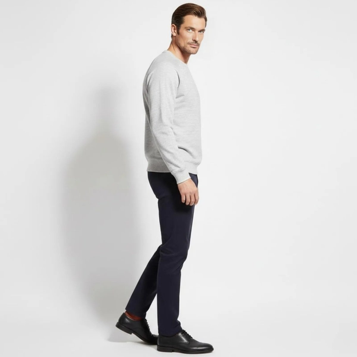 Side profile of a male model walking in the Kouvr Deacon Crewneck Sweatshirt in heather light grey, showing the garment's fit and silhouette.