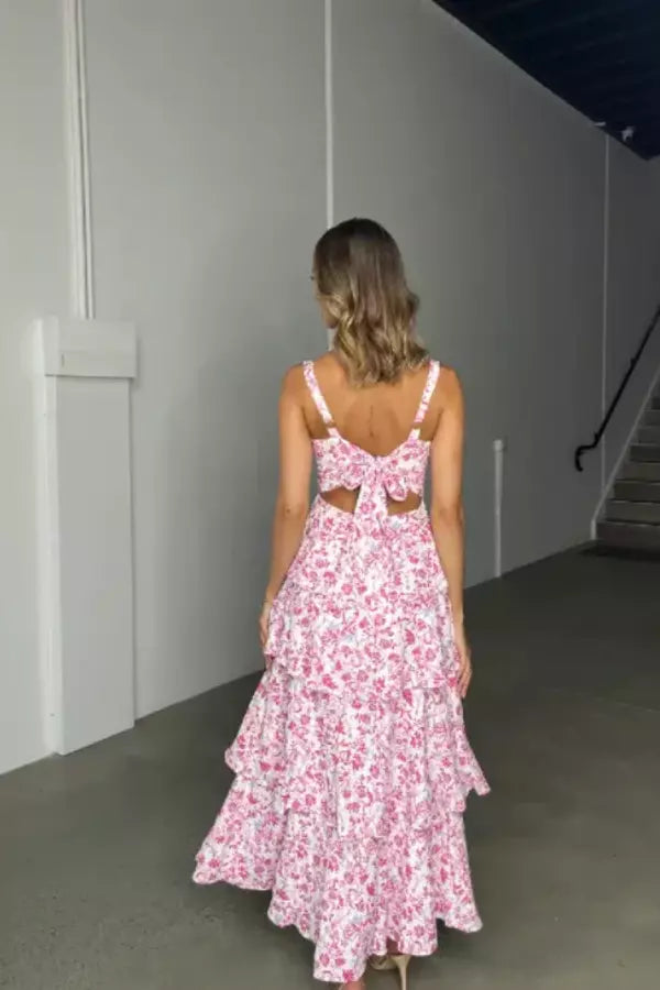 Model wearing the Kouvr Denise pink floral tiered midi dress with a square neckline and open-back bow detail at a garden party