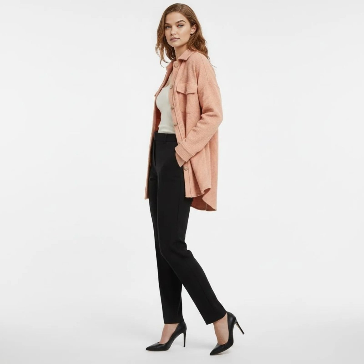 Side profile of a model wearing the Kouvr Donna apricot shirt jacket to show its length and relaxed silhouette with hands in pockets.