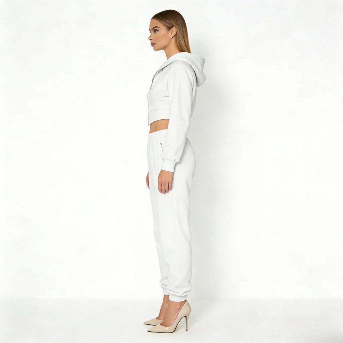 Side profile of a woman in a luxury white two-piece loungewear set showing the tailored fit of the cropped hoodie and matching sweatpants from Kouvr.