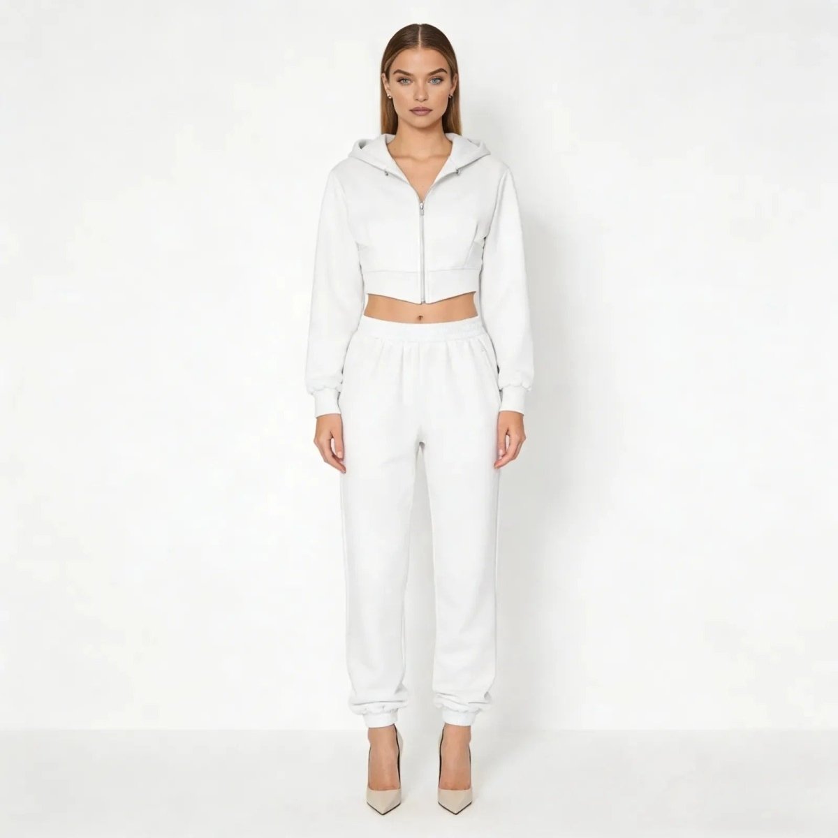 Model wearing the Kouvr Ellaine women's white tracksuit set, featuring a cropped corset zip-up hoodie and high-waisted joggers, styled with heels.