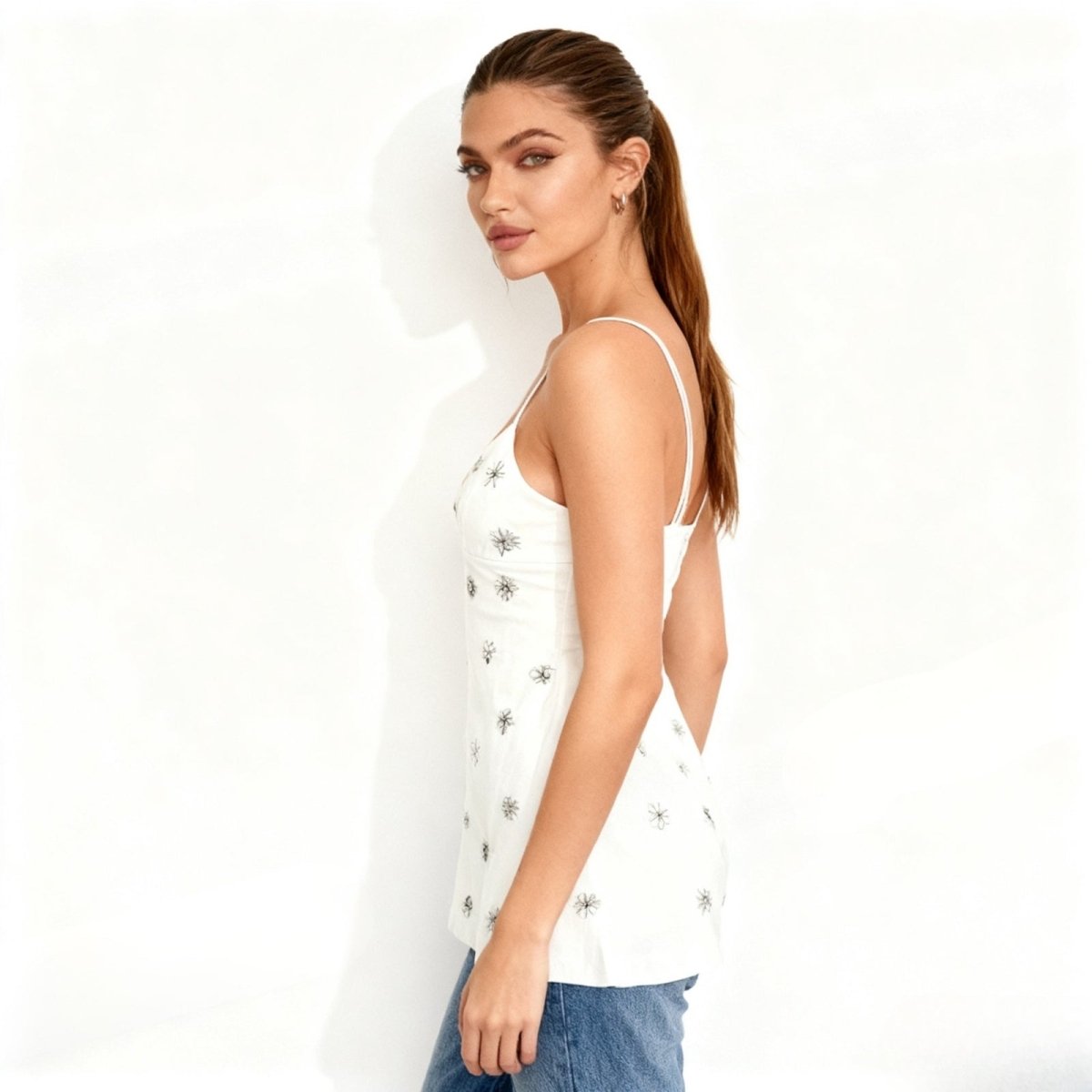 Model wearing the Kouvr white embellished tank top styled with blue jeans, highlighting the V-neck fit and floral rhinestone details for a bridal or party look.
