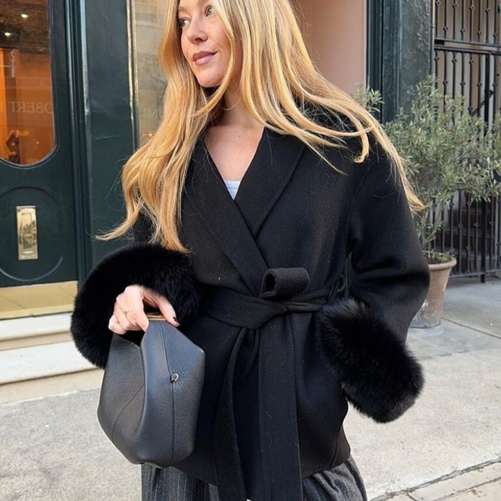 Woman styling the Kouvr Emma  black fur cuff jacket on a city street, paired with a black handbag and grey trousers.