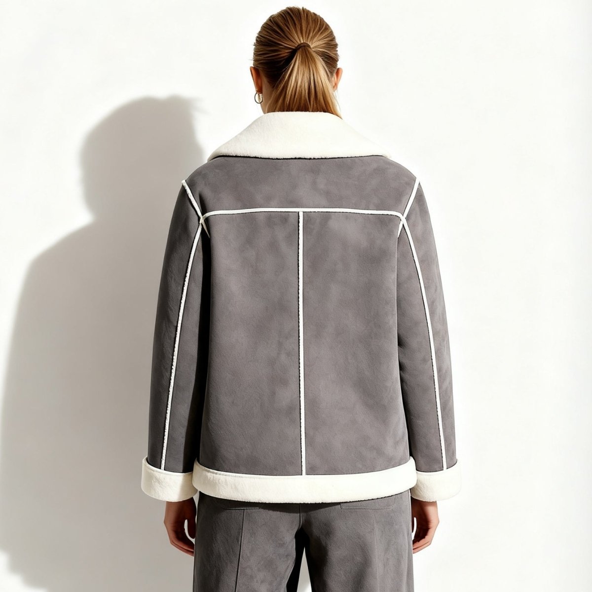 Back view of a model wearing the Kouvr Esmeralda grey shearling jacket, showcasing the white seam detailing.
