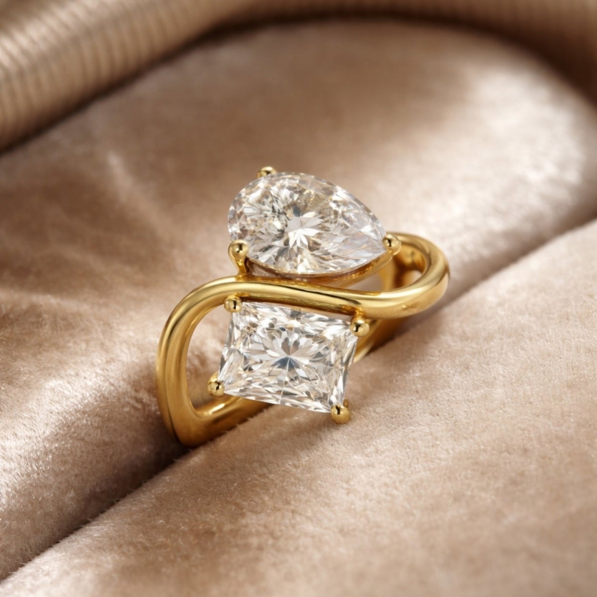 The Kouvr Toi et Moi pear and princess cut diamond ring resting on a luxurious beige velvet surface, showcasing its sparkle.