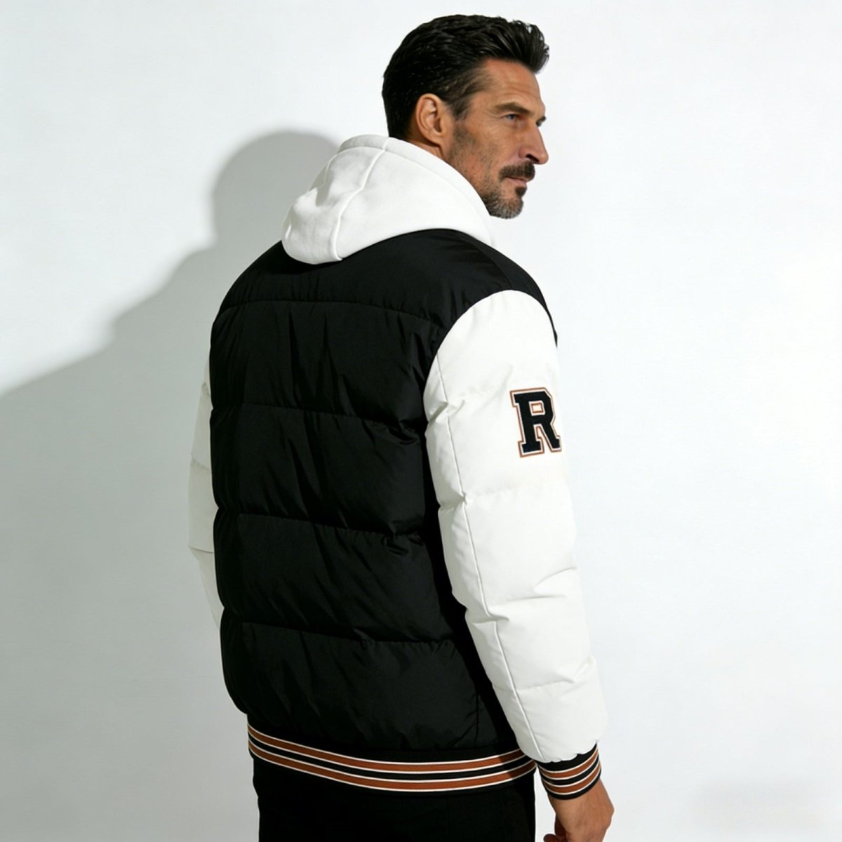 Back view of a man in the Kouvr Fashion 'Angelo' varsity puffer jacket, highlighting the quilted black body, white sleeves, and white hood.