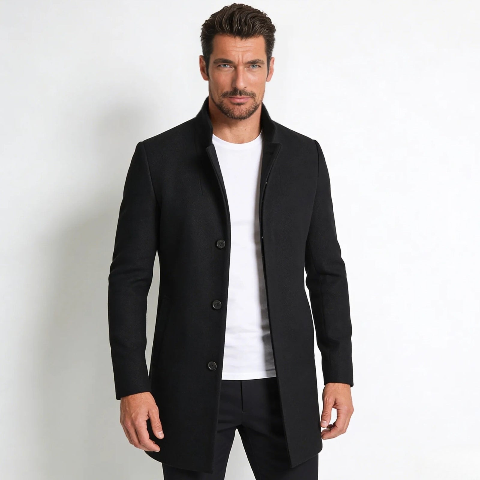 Male model wearing the Kouvr Fashion Archie black wool stand collar overcoat, buttoned, styled with a white t-shirt and black trousers against a white background.