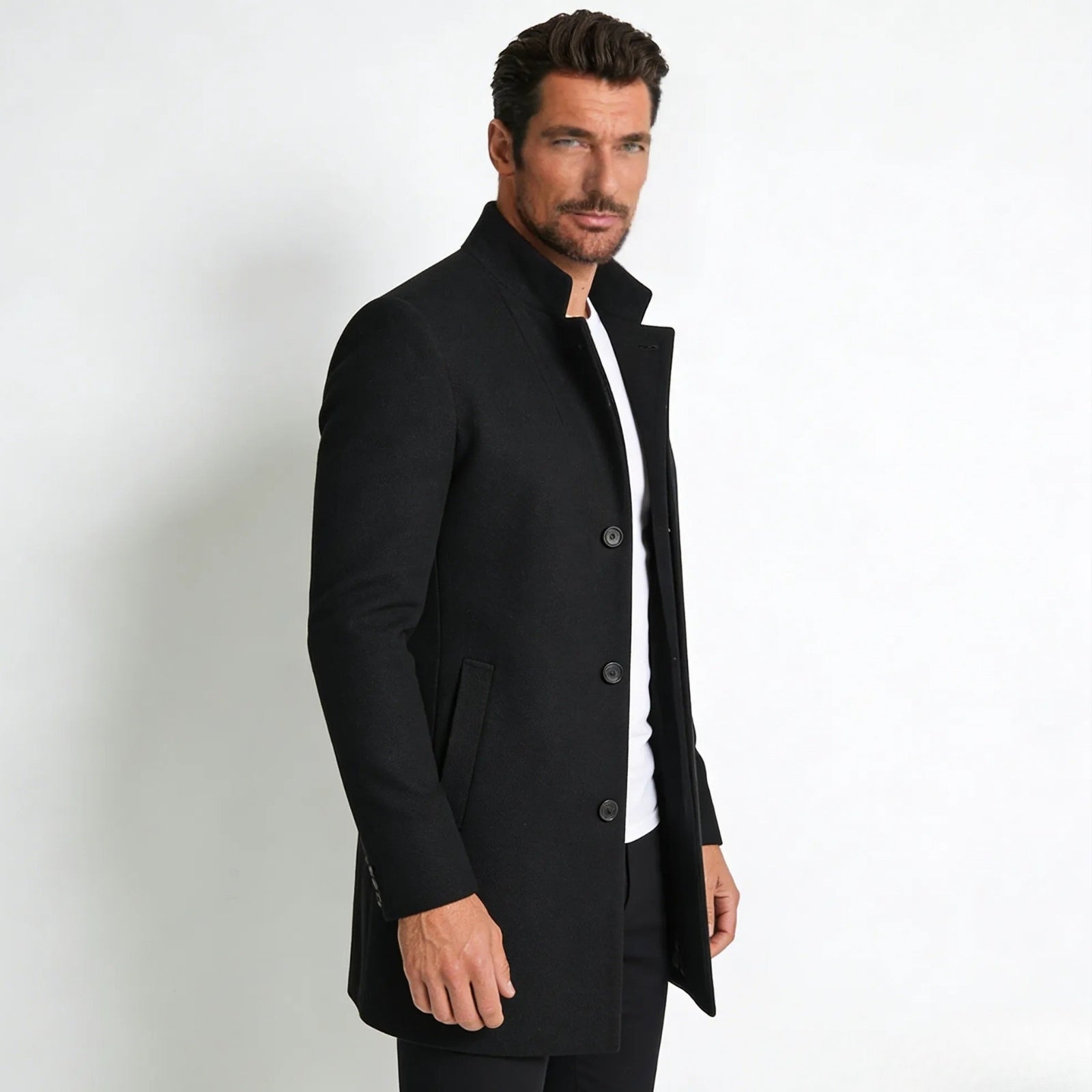 Side profile of a male model in a Kouvr Fashion slim fit black wool overcoat, showing the tailored silhouette and mid-length cut.