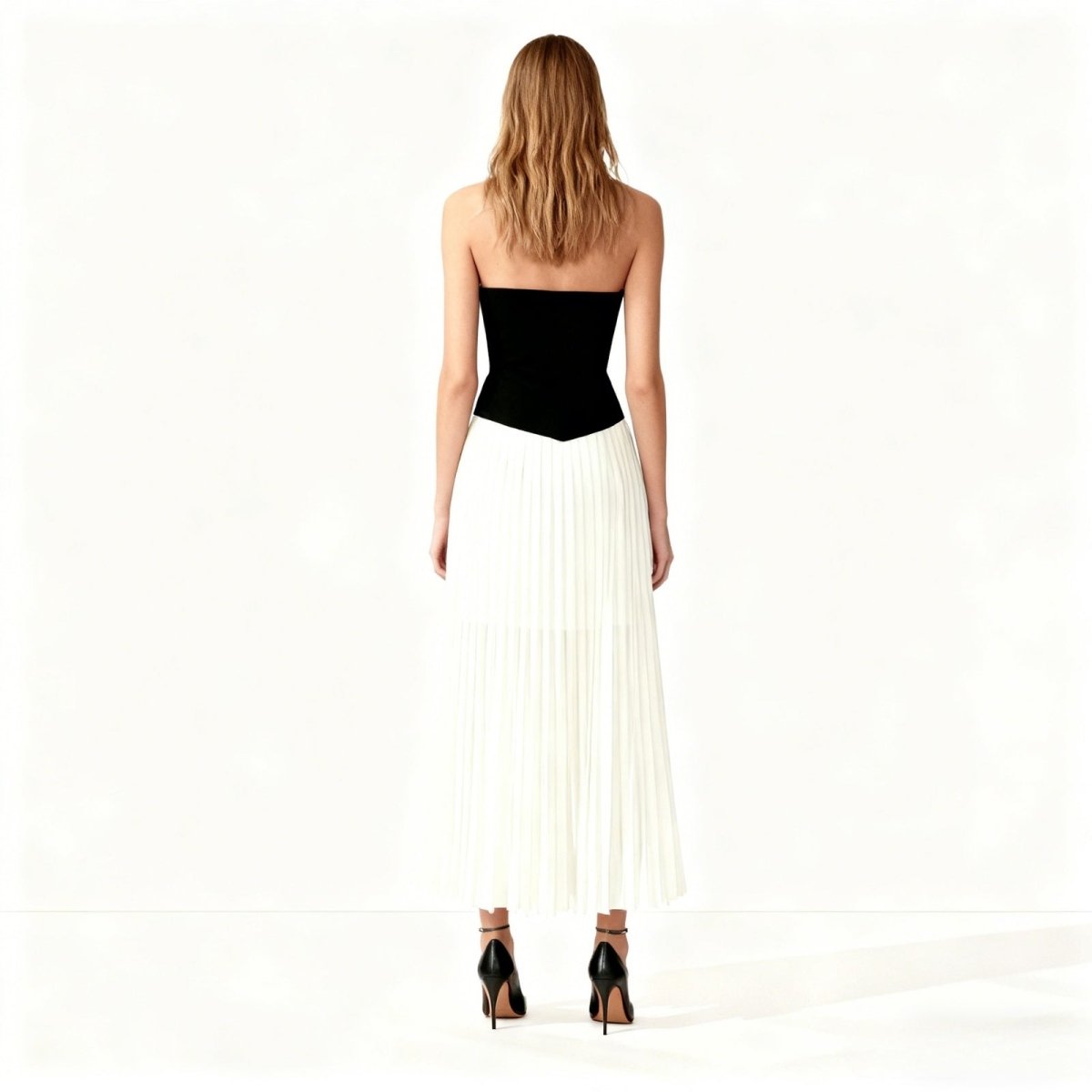 Woman wearing a black strapless top and white pleated skirt on a white background