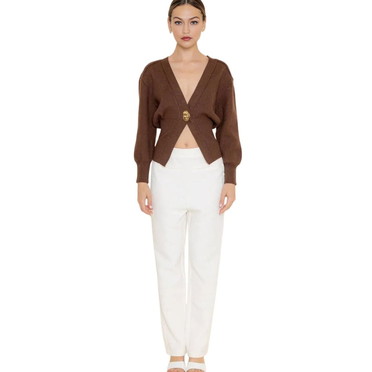 Model wearing the Kouvr Avaline cropped brown cardigan with a gold clasp, paired with white trousers.