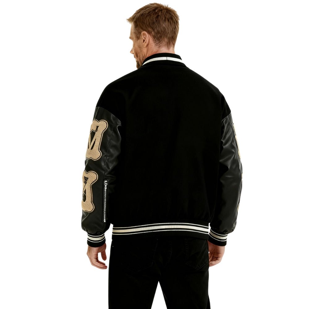 Person wearing a black Kouvr jacket with gold designs on the back, standing against a white background