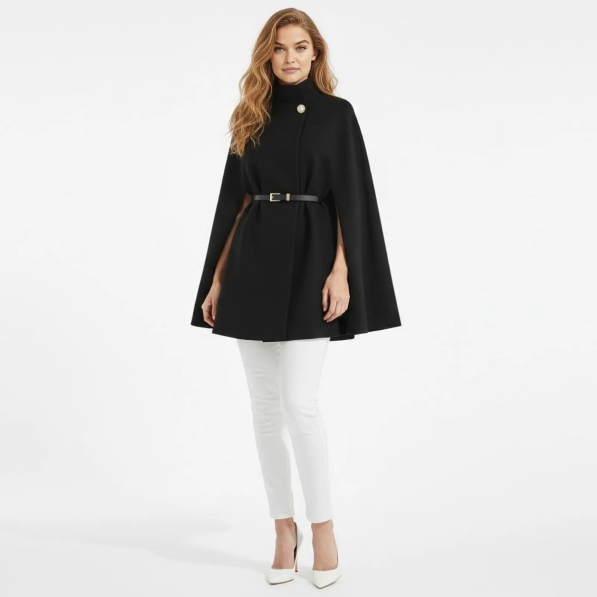 Woman wearing the Kouvr Fashion black high-neck belted cape coat, styled with white trousers and white heels, standing forward against a white background.